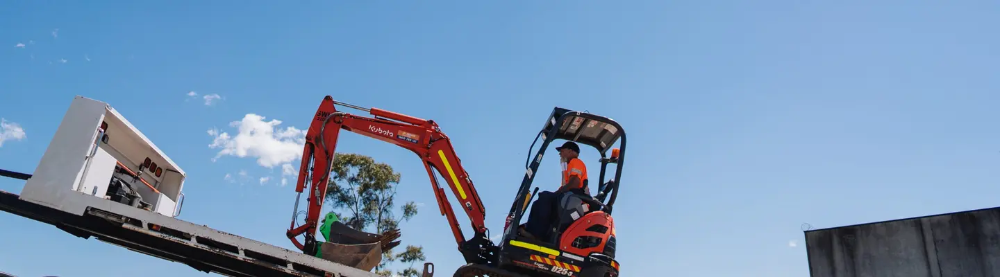 A man operating a tracked trailer vehicle on a construction site, transporting materials across rough terrain.