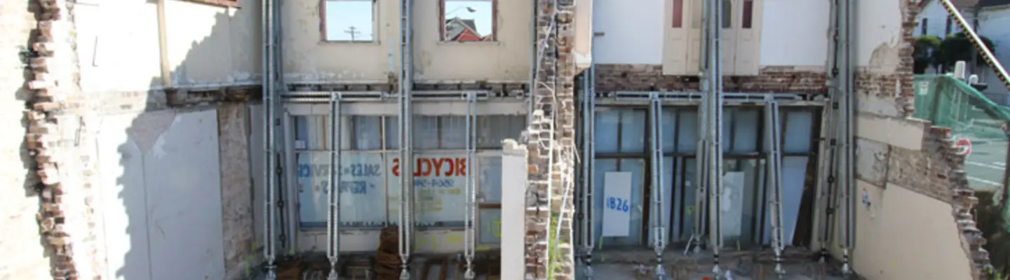 Worker on building facade using machinery and equipment, with structural props in place for support and safety.