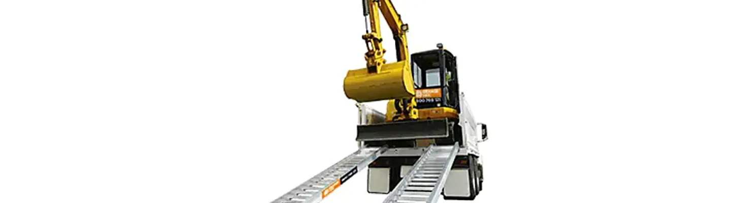 A compact excavator positioned on a trailer ramp, ready for loading or transport against a plain background.