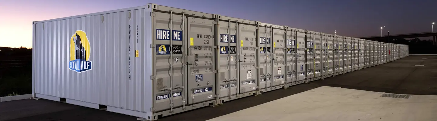 Long row of RoyalWolf branded storage containers lined up in an outdoor yard at dusk.