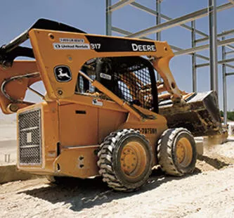 yellow john deere skid steer on jobsite in front of framed building