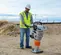 Orange and silver Multiquip heavy-duty vibratory rammer being used to tamper soil