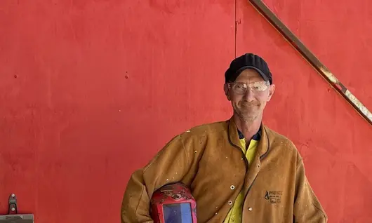 Man using welding tools at a worksite, wearing protective gear and performing metalwork as part of a construction project.