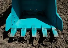 Bucket roller resting on sand at a construction site, used for compacting soil with safety barriers in the background.