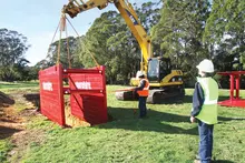Workers lowering a protective box into an excavation site to ensure trench safety during construction work.