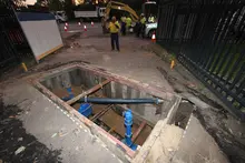  Workers at excavation site managing water main pit repairs with safety barriers and equipment in place.