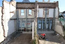 Worker on building facade using machinery and equipment, with structural props in place for support and safety.