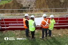 Four engineers, wearing their safety equipment, review blueprints for an excavation project while standing in front of a Steel Shoring Box equipped with an Edge Protection System, showcasing one of our Temporary Works Solutions services.