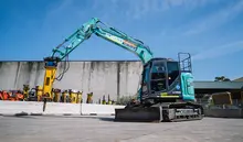 Teal blue tracked Kobelco excavator with a rock breaker attachment at a United Rentals hire yard