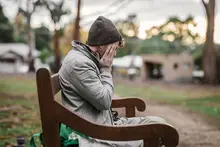 Sad man sitting alone on a park bench, appearing deep in thought during a quiet moment outdoors.