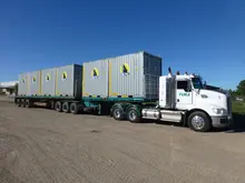 A truck loaded with stacked shipping containers driving on a highway, ready for delivery to a storage or shipping facility.
